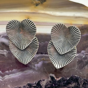 May include: A pair of silver earrings with a layered heart design. The hearts have a textured, sunburst pattern.