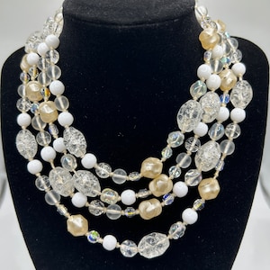 May include: A multi-strand necklace made of clear, white, and cream-coloured glass beads. The beads are of various sizes and shapes, including round, oval, and faceted.