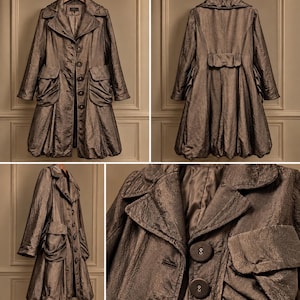 May include: A metallic bronze-toned coat featuring a structured collar, long sleeves, and a button-front closure. The garment includes two large, gathered patch pockets on the front and a bubble-style hemline, showcasing a textured, crinkled fabric finish.