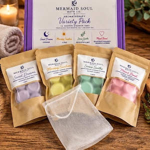 May include: A Mermaid Soul Bath Co. aromatherapy variety pack box containing 16 shower steamer tabs in four scents: Sweet Dreams, Morning Sunshine, Sinus Soothe, and Mood Boost. Four individual kraft paper pouches hold purple, yellow, green, and pink tabs, accompanied by a white mesh bag.