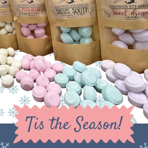 Può includere: Un set di 12 pastiglie effervescenti per la doccia in quattro fragranze diverse: Mood Boost, Sinus Sooth, Sweet Dream e Limone & Lime. Le pastiglie sono confezionate in sacchetti di plastica trasparente con etichette di carta marrone. Le etichette presentano un logo di sirena e il nome della fragranza. Il testo "Tis the Season!" è stampato su uno sfondo rosa e blu con fiocchi di neve. Il testo "12 steamers Net wt. 7 oz" è stampato sotto il testo "Tis the Season!"