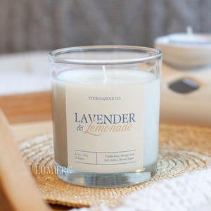 K&ouml;nnte beinhalten: Ein klares Glas mit wei&szlig;em Wachs gef&uuml;llt. Das Etikett lautet "Lavender & Lemonade" mit dem Text "Your Candle Co." dar&uuml;ber. Die Kerze steht auf einer gewebten Matte.