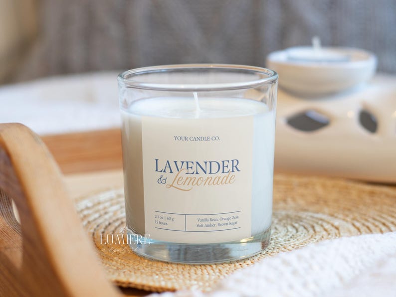 K&ouml;nnte beinhalten: Ein klares Glas mit wei&szlig;em Wachs gef&uuml;llt. Das Etikett lautet "Lavender & Lemonade" mit dem Text "Your Candle Co." dar&uuml;ber. Die Kerze steht auf einer gewebten Matte.