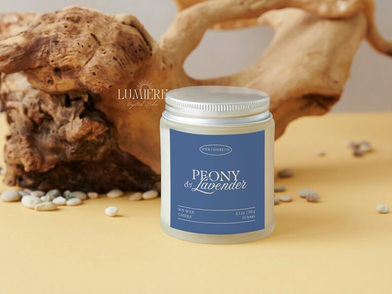 K&ouml;nnte beinhalten: Ein zylindrisches Kerzenglas mit silbernem Deckel und blauem Etikett. Auf dem Etikett steht "PEONY & Lavender" und "Soy Wax Candle". Das Glas enth&auml;lt 60 g Wachs und hat eine Brenndauer von 11 Stunden. Im Hintergrund Treibholz und kleine Steine.