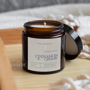 K&ouml;nnte beinhalten: Eine Sojawachs-Kerze in einem braunen Glas mit schwarzem Deckel. Auf dem Etikett steht "Cinnamon & Vanilla" und die Inhaltsstoffe sind aufgelistet. Die Kerze steht auf einem Holztablett, im Hintergrund ein wei&szlig;er Stoff. Das Glas enth&auml;lt 60 g Wachs.