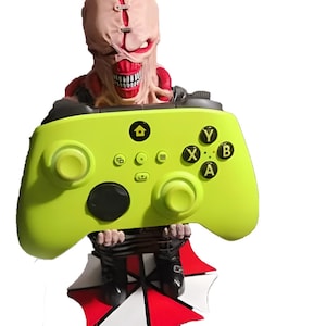 May include: A lime green video game controller with black buttons and a character figure. The figure has a pale face, red accents, and a large open mouth. The controller has the letters Y, X, B, and A on it.