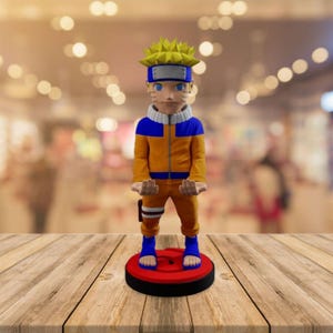 May include: A figurine of a character with spiky yellow hair, blue eyes, and a blue headband. The character wears an orange and blue outfit and stands on a red and black base. The figurine is displayed on a wooden surface.