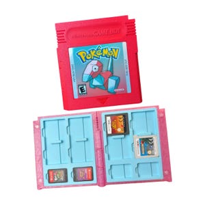 May include: A red Nintendo Game Boy Pokémon cartridge with the text "Pokémon" and a geometric character. Below, a pink game cartridge holder with blue slots holds several game cartridges.