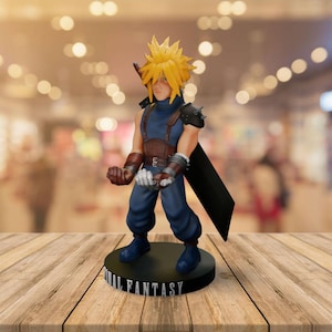May include: A figurine of Cloud Strife from Final Fantasy, featuring spiky blonde hair, a blue outfit, and a black sword. The figure stands on a black base with "FINAL FANTASY" in white lettering. The figurine is posed with clenched fists.