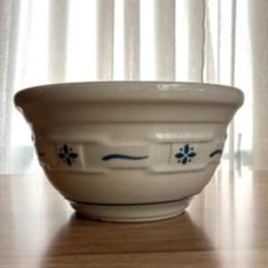 May include: A white ceramic mixing bowl featuring a raised basket-weave texture around the exterior. The bowl is decorated with small, blue, four-petaled floral motifs and thin, horizontal blue wavy lines encircling the middle section.