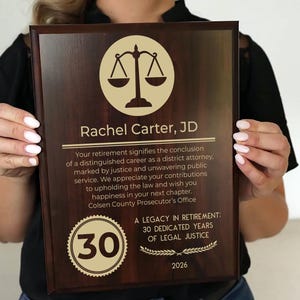 May include: A dark brown wooden plaque with gold lettering. The plaque has a gold circle with the number 30 in it. The text on the plaque reads "Rachel Carter, JD" and "A Legacy in Retirement: 30 Dedicated Years of Legal Justice".