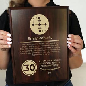 May include: A wooden retirement plaque with gold-colored text and graphics. The plaque features the name "Emily Roberts", a diagram, and the text "A LEGACY IN RETIREMENT: 30 DEDICATED YEARS OF CODING INNOVATION 2026".