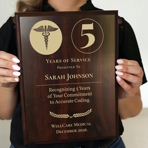 May include: A wooden plaque with gold lettering and accents, presented to Sarah Johnson for 5 years of service. The plaque includes the Wellcare Medical logo, a caduceus symbol, and the date December 2026.