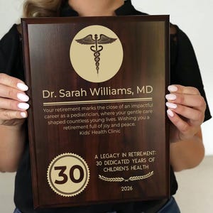 May include: A wooden plaque with a gold medical symbol and text. The plaque reads "Dr. Sarah Williams, MD" and includes a message about retirement. A gold seal displays the number "30" and the text "A Legacy in Retirement: 30 Dedicated Years of Children's Health".