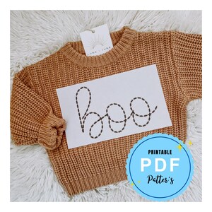 May include: A printable PDF pattern for a "boo" embroidery design. The pattern is displayed on a brown sweater with a white tag that says "Luna June".