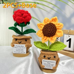 May include: Two crocheted potted plants, one with a red rose and the other with a yellow sunflower. The rose pot has a sign that reads "Positive Rose Where roses bloom, so does hope. Keep growing, bloom your own way." The sunflower pot has a sign that reads "Emotional Support Plant Life can be tough sometimes, but remember so are you!"
