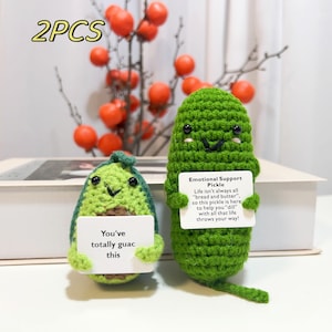 May include: Two crocheted plush toys shaped like an avocado and a pickle. The avocado is holding a card that says "You've totally guac this". The pickle is holding a card that says "Emotional Support Pickle. Life isn't always all "bread and butter", so this pickle is here to help you "dill" with all that life throws your way!"