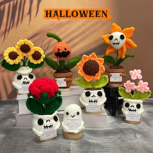 Peut inclure: Une collection de décorations d'Halloween faites à la main au crochet. L'ensemble comprend diverses fleurs et un fantôme, chacun dans un pot en forme de crâne. Les fleurs sont dans des tons de jaune, d'orange, de rouge et de rose. Le mot "HALLOWEEN" est affiché en haut.