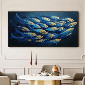 Könnte beinhalten: Abstrakte Malerei eines Fischschwarms. Die Fische sind blau mit goldenen Akzenten und schwimmen vor einem dunkelblauen Hintergrund. Das Kunstwerk ist gerahmt und hängt über einem runden Tisch und zwei Sesseln.
