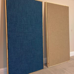 May include: Two rectangular acoustic panels with wooden frames. One panel is covered in a textured dark blue fabric, while the other is covered in a textured beige fabric. Both panels are tall, vertical, and feature a clean, simple design.