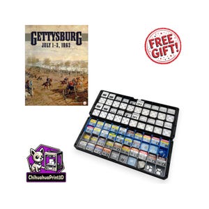 May include: A board game titled "Gettysburg July 1-3, 1863" with a historical battle scene on the cover. The game is open, revealing game pieces in a black case. A "Free Gift!" sticker is visible.