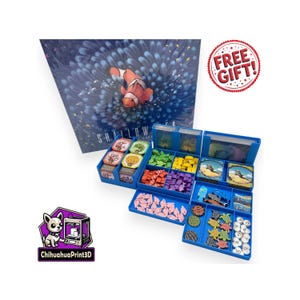 May include: A board game called "Shallow Sea" featuring a clownfish illustration. The game components, including cards and pieces, are stored in blue containers. A "FREE GIFT!" sticker is also present.