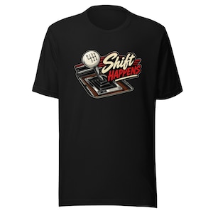 May include: A black short-sleeved t-shirt featuring a graphic of a manual car gear shifter with a white knob showing a six-speed pattern. The text Shift HAPPENS is printed in a stylised cream and red font next to the gear shifter illustration.