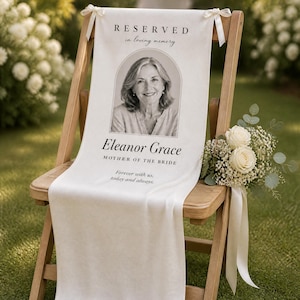 Puede incluir: Un letrero conmemorativo de tela blanca sobre una silla plegable de madera, con un retrato en blanco y negro de una mujer en un marco arqueado, con el texto RESERVED in loving memory, Eleanor Grace, MOTHER OF THE BRIDE, Forever with us, today and always.