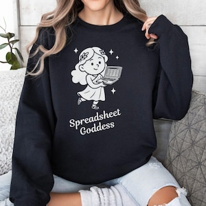 May include: Black sweatshirt featuring a white graphic of a cartoon figure holding a laptop with a spreadsheet. The text "Spreadsheet Goddess" is below the graphic. The sweatshirt is a crew neck style.