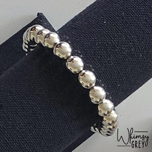 May include: A silver beaded bracelet with a simple design. The bracelet is made of small, round beads that are connected together to form a continuous loop. The beads are smooth and shiny, and they reflect light beautifully.