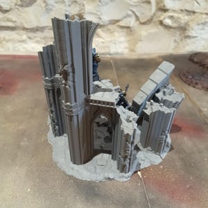 Pode incluir: Um modelo em miniatura cinzento de uma catedral gótica em ruínas. O modelo apresenta elementos arquitetónicos detalhados, incluindo arcos, colunas e paredes em ruínas. A miniatura é provavelmente para jogos de mesa ou construção de modelos.