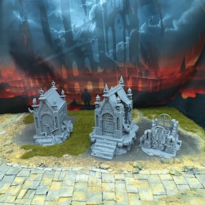 Op de afbeelding: Drie grijze miniatuur crypten met gedetailleerde architectonische kenmerken, geplaatst op een grasachtige basis met een geplaveid pad op de voorgrond. De achtergrond toont een donker, onheilspellend landschap met een kasteelsilhouet.