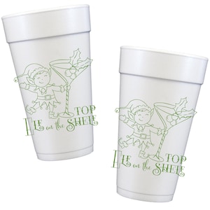 May include: Two white foam cups with a green illustration of a cartoon elf and a martini glass with holly. The text "Top on the Shelf" is printed in green below the illustration. The cups are designed for beverages.