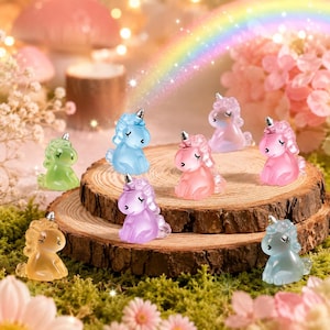 May include: A collection of small, translucent unicorn figurines in various pastel colors including blue, pink, purple, green, yellow, and light blue. Each unicorn features a silver-colored horn and closed eyes, arranged on a wooden slice.