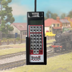 May include: A black handheld model train controller with a red and white display. The display shows the text "Digitrax" and has buttons labelled "FUNC", "ME", "LOCO", "SWCH", "DISP", "PROG", "FIND", "EXIT", "ENTER", "BACK", "OPTN", "CLOC", "ENDA", and "STOP". The controller has a black knob on the top and a black antenna.