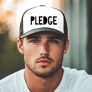 May include: A black and white trucker hat with the word "PLEDGE" in black letters on the front.