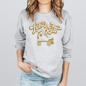 May include: A gray sweatshirt with the text "Let's Roll" in gold lettering and a gold silhouette of a roller skate.