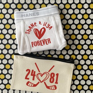 May include: White Hanes boxer briefs with the names "Shane & Ilya" and the word "Forever" in red. A cream-colored zippered pouch features hockey sticks, a heart, and the numbers "24 81" in red.