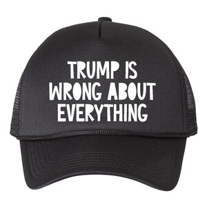 May include: Black trucker hat with white text that reads "TRUMP IS WRONG ABOUT EVERYTHING." The hat has a curved brim and a mesh back.