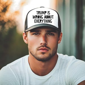 May include: A black and white trucker hat with the text "TRUMP IS WRONG ABOUT EVERYTHING" in bold, black letters. The hat has a white front panel and a black mesh back. The hat is worn by a person wearing a white t-shirt.