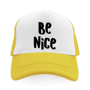 May include: A yellow and white trucker hat with the words "Be Nice" in black, bold lettering across the front. The hat has a yellow brim and mesh backing.