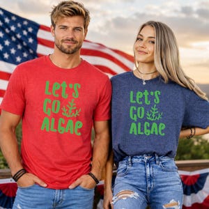 May include: A red short-sleeved t-shirt and a navy blue short-sleeved t-shirt, both featuring the green text "Let's GO ALGAE" with a small seaweed graphic. The shirts are made of a heathered fabric and have a crew neckline and short sleeves.