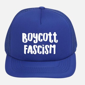 May include: A royal blue trucker hat with white text that reads "BOYCOTT FASCISM". The hat features a mesh back and a curved brim. The text is in a bold, sans-serif font.