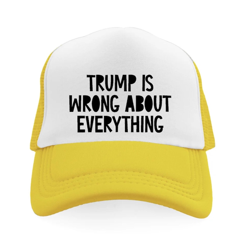 May include: A yellow and white trucker hat with the text "TRUMP IS WRONG ABOUT EVERYTHING" in black block letters. The hat has a yellow brim and mesh backing.