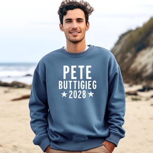 May include: A blue sweatshirt with white text that reads "Pete Buttigieg 2028" with a star on either side of the year.