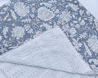 May include: A blue and white floral kantha quilt with a white background and a blue floral pattern. The quilt is folded in half and the stitching is visible.
