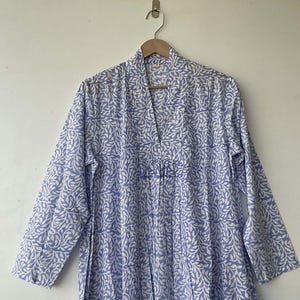 May include: A long, light blue robe with a white leaf pattern, hanging on a wooden hanger. The robe has a V-neck and long sleeves. The fabric is lightweight and appears to be cotton or a similar material.