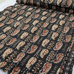 Op de afbeelding: Een zwarte kantha-deken met een paisley-patroon in tinten bruin, crème en rood. De deken is met de hand gestikt en heeft een textuur.
