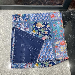 May include: A patchwork quilt with a variety of blue floral patterns and a solid navy blue backing. The quilt is stitched with white thread and has a scalloped edge. The quilt is folded in half.