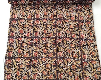 May include: A brown kantha quilt with a floral pattern in shades of red, yellow, and white. The quilt is folded in half and is lying on a white surface.